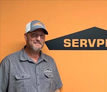 Male employee standing in front of SERVPRO orange wall, grey shirt